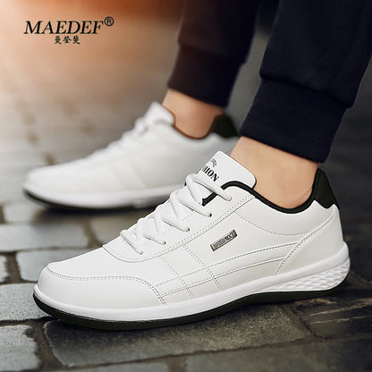 White sneakers with black accents worn by a person on a stone surface, with MAEDEF branding.