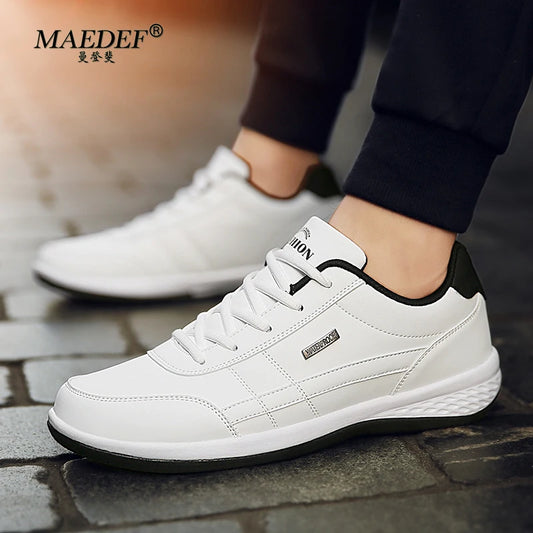 White sneakers with black accents worn by a person on a stone surface, with MAEDEF branding.